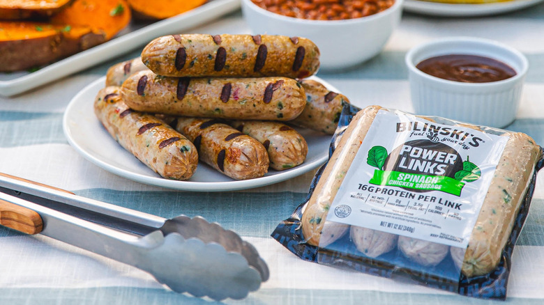 A package of Bilinski's Spinach Chicken Sausage sits next to the cooked product on a plate.
