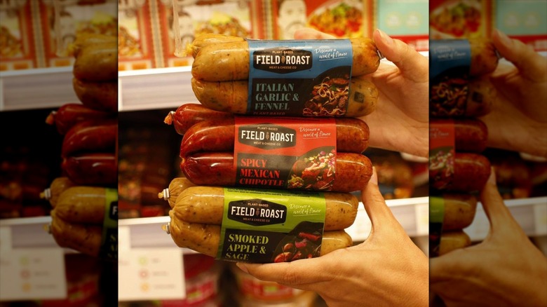 A person is holding three varieties of Field Roast sausages.