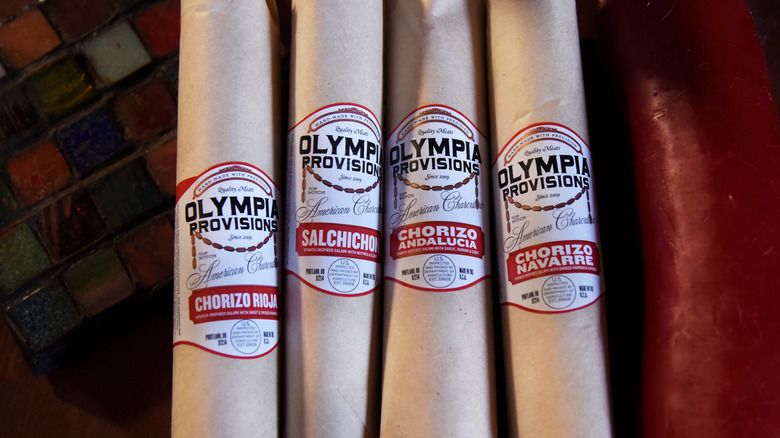 Four sausages are wrapped in paper and labeled with Olympia Provisions stickers.