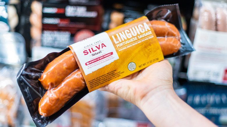 A hand is holding Silva brand linguiça in a grocery store.