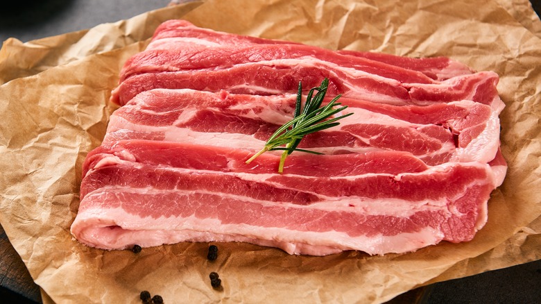 Raw pork belly with a sprig of rosemary on parchment paper