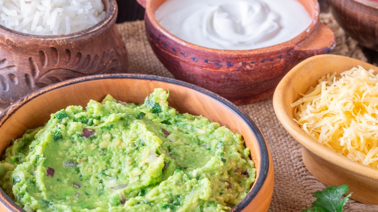 Small bowls full of guacamole, shredded cheese, and sour cream