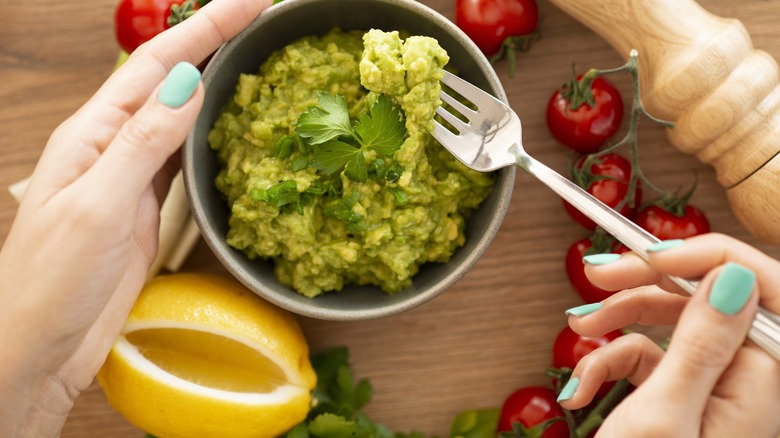 Hand mixing small bowl of guacamole with lemon and other fresh ingredients