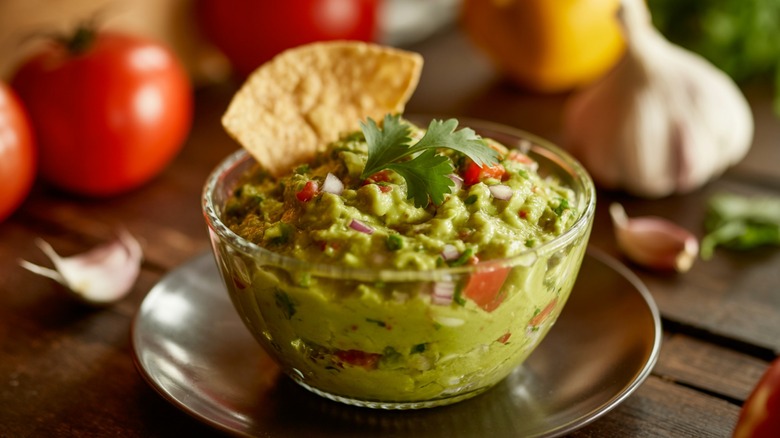 Glass bowl of fresh guacamole with a tortilla chip sticking out