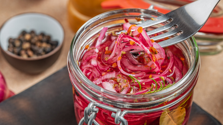 Fork extracting pickled red onions from small glass jar