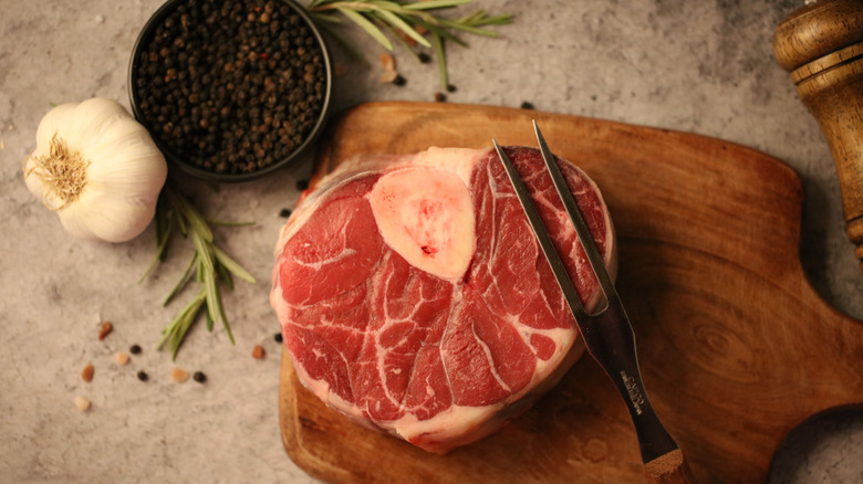 Raw beef shank with a carving fork on a wooden cutting board