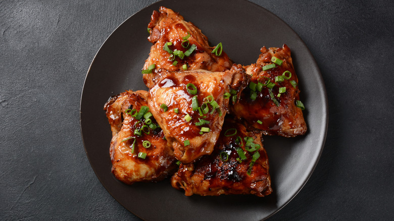 Adobo chicken thighs with scallions on a black plate