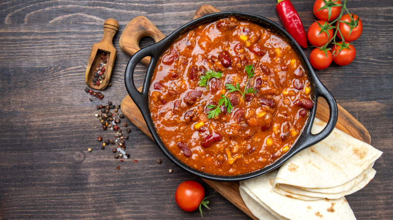 Chili con carne in an iron skillet on a wooden cutting board with folded tortillas