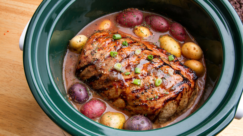A roast with small potatoes and gravy in a slow cooker