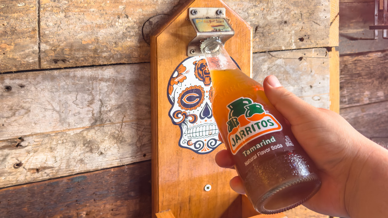 Hand using opener to pop open a bottle of Jarritos Tamarind Soda