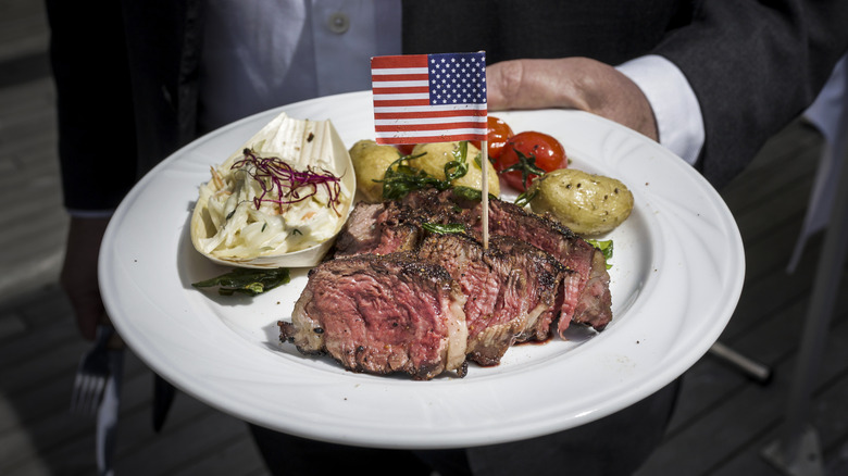 Hand holding steak dinner plate with an American flag