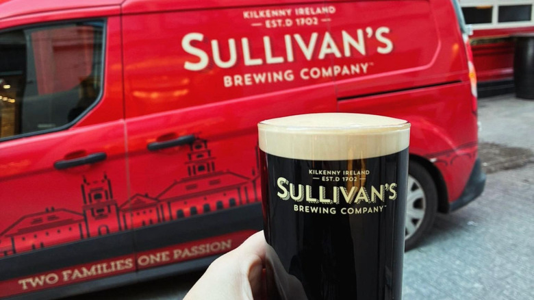 Hand holding glass of Sullivan's Black Marble Stout in front of a company van