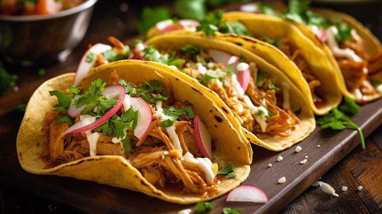 Four chicken tacos topped with red onion and parsley