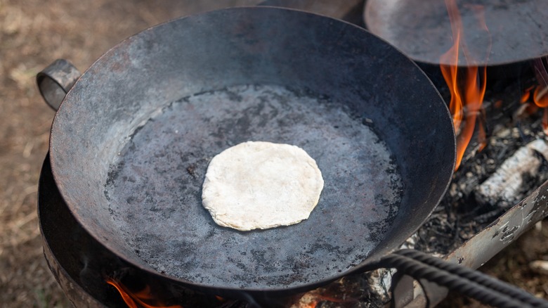 A tortilla cooking in a skillet over an open flame