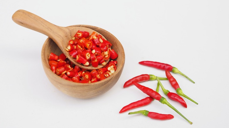 Chopped chillis in a wooden bowl with a few whole ones beside it