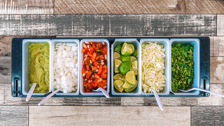 Ingredients for taco toppings lined up in containers without a lid