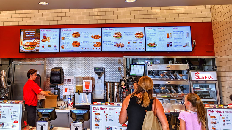 Customers reading over a Chick-fil-A menu behind the registers