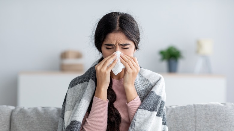 sick woman blowing nose into tissue