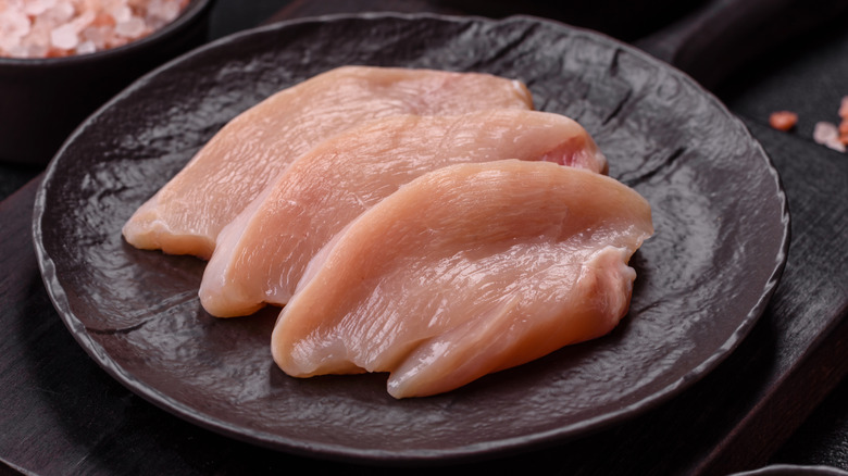 Filets of chicken breast on a dark platter near a dish of salt