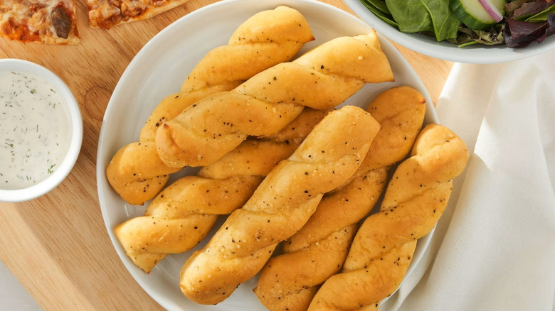 A bowl of Great Value Garlic Bread Sticks beside a salad and pizza.