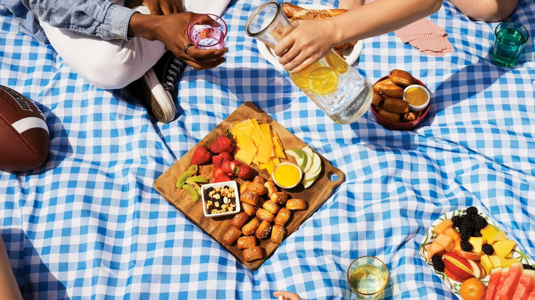 A plate and a bowl of SuperPretzel Soft pretzel bites at a picnic, with sliced fruit and cheese.