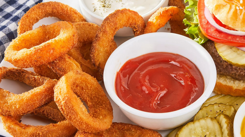 A plate full of Great Value onion rings next to a burger and two bowls of dip.
