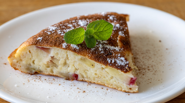 A slice of an apple omelet with a piece of mint on a white plate