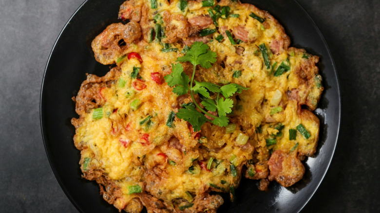Thai omelet with pork, scallions, and herbs on a black plate