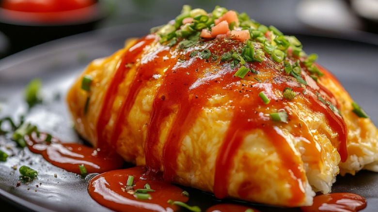 Close up of the Japenese dish omurice, a thin omelet over fried rice with red sauce and chives on top
