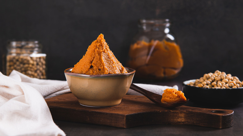 Miso paste is piled in a small bowl on a wooden cutting board next to a small wooden spoon with miso paste