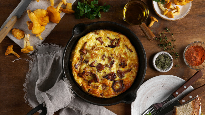 Chanterelle mushrooms rest to the side of a cast iron skillet with a baked mushroom omelet