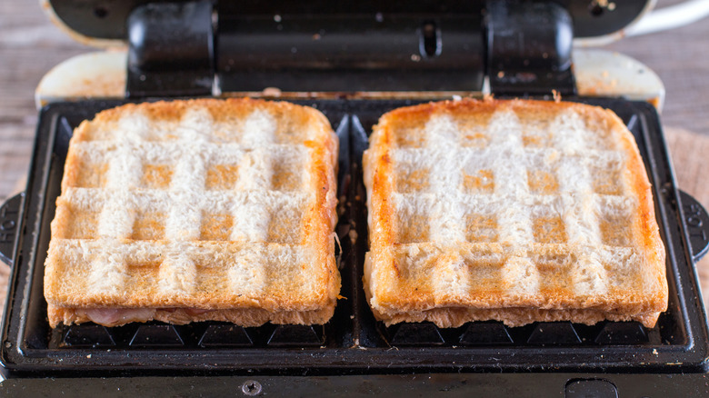 Two sandwiches are toasted in a waffle iron