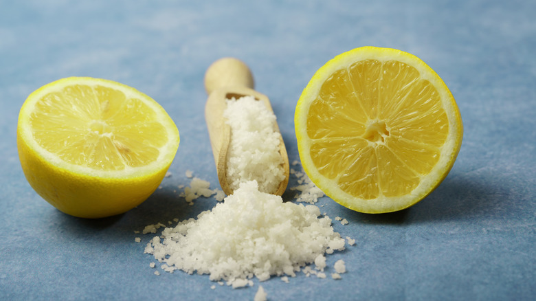 Two cut lemon halves sit on either side of a wooden scoop filled with salt and a small pile of salt