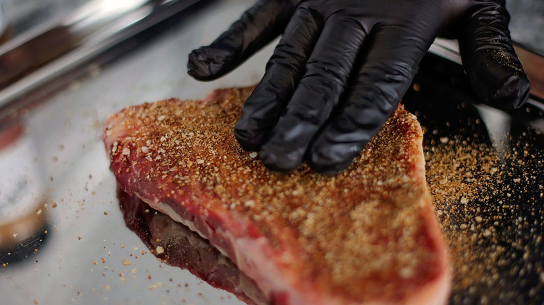 Gloved hand rubbing seasoning into a steak