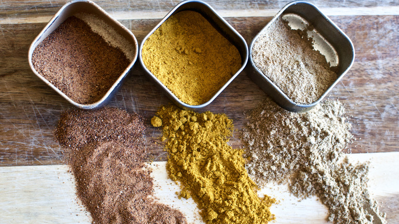 Three different spices in metal containers, spilling out, on a wooden surface