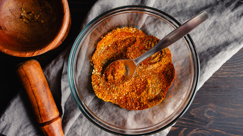 Top down view of berbere in a glass bowl with a metal spoon and wooden mortar and pestle