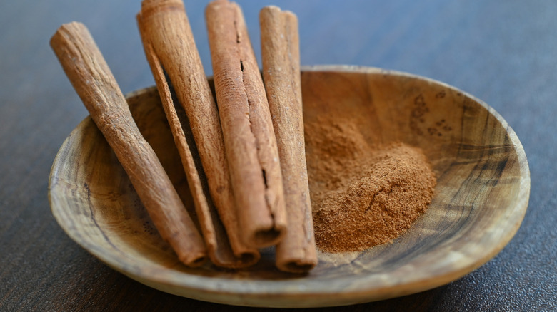 Some cinnamon sticks and ground cinnamon in a wooden bowl