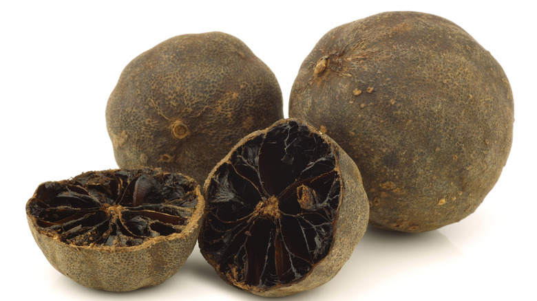 Two whole black limes and another that has been cut in half, it is black inside