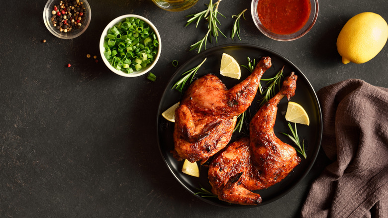 Two chicken halves with scallions, peppercorns and lemon on a black surface