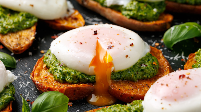 A poached egg on pesto and toast with some leaves of basil