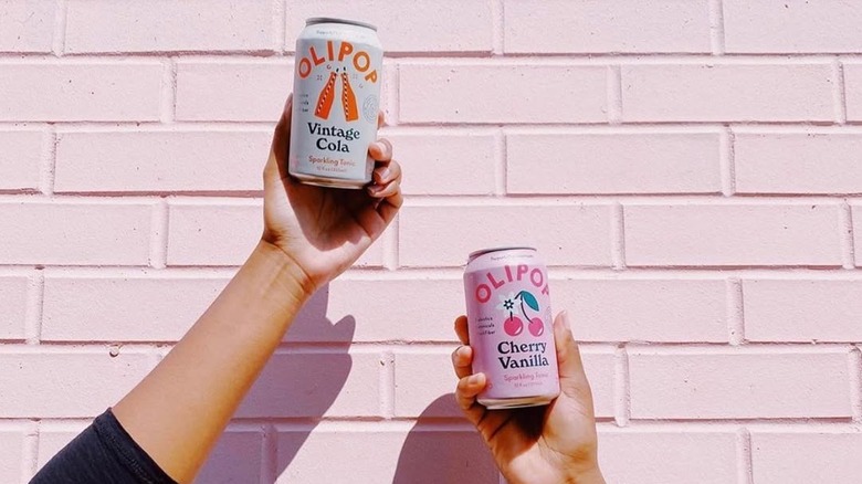 Two hands holding two cans of OLIPOP
