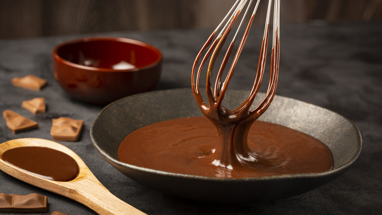 a whisk in chocolate ganache with a wooden spoon and red bowl
