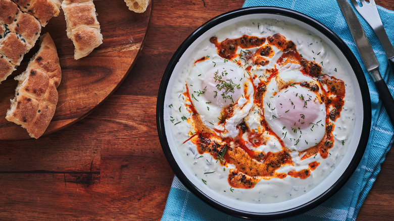 Poached eggs sit in a dish of herbed yogurt and chili oil