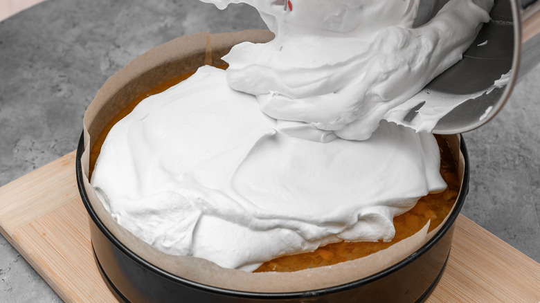 Whipped cream is piled on top of a cake inside of a parchment-lined cake pan