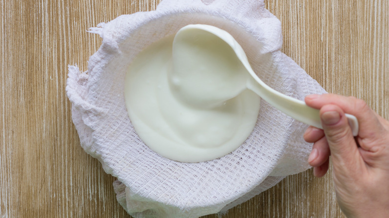 A person ladles homemade yogurt into a bowl lined with cheesecloth