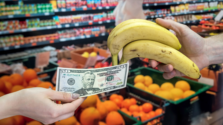 Hand giving money for bananas in produce section