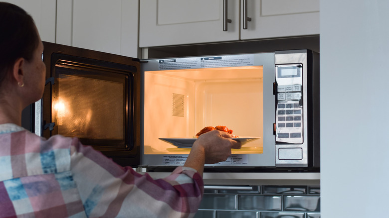 A woman placing a plate with food into a microwave