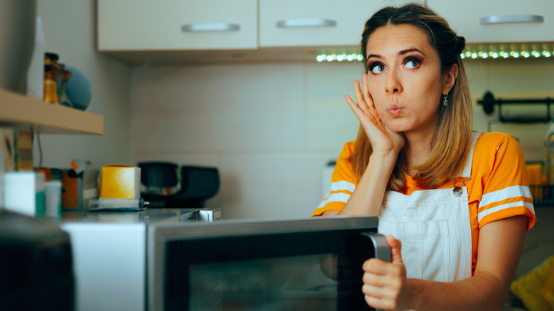 A surprised woman opening a microwave door