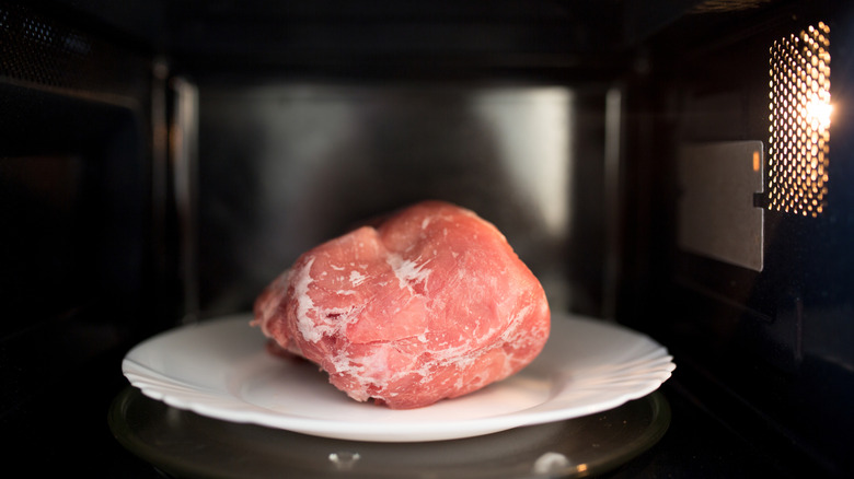 A close-up of a large chunk of meat defrosting in a microwave