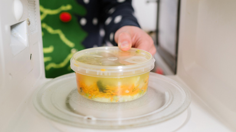 A plastic container of food going into a microwave